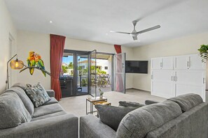 A modern living room with grey sofas, a ceiling fan, a flat-screen TV, and a sliding glass door leading to an outdoor area. - Mambo Stay,  luxury apartment with Hot Tub (Willemstad)