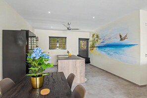 A modern kitchen with a wooden island, a ceiling fan, and a mural of a beach scene. - Mambo Stay,  luxury apartment with Hot Tub (Willemstad)