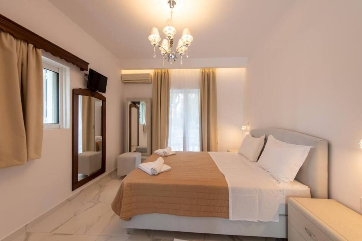 A hotel room with a bed, a television, a mirror, a chandelier, and a window with curtains.