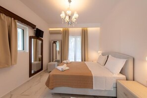Une chambre d’hôtel avec un lit, une télévision, un miroir, un lustre et une fenêtre avec des rideaux.