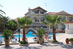 A resort with a swimming pool, palm trees, and a multi-story building with balconies.