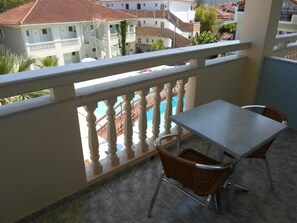 Un balcon avec une table et des chaises, une piscine en arrière-plan et une vue sur les bâtiments environnants.