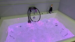 A bathtub with water jets, a bottle of champagne, and two glasses on the side. - Apartament z Jacuzzi Kraków GREY Miodowa (Kraków)