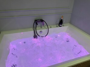 Eine Badewanne mit Wasserdüsen, eine Champagnerflasche und zwei Gläser am Rand.