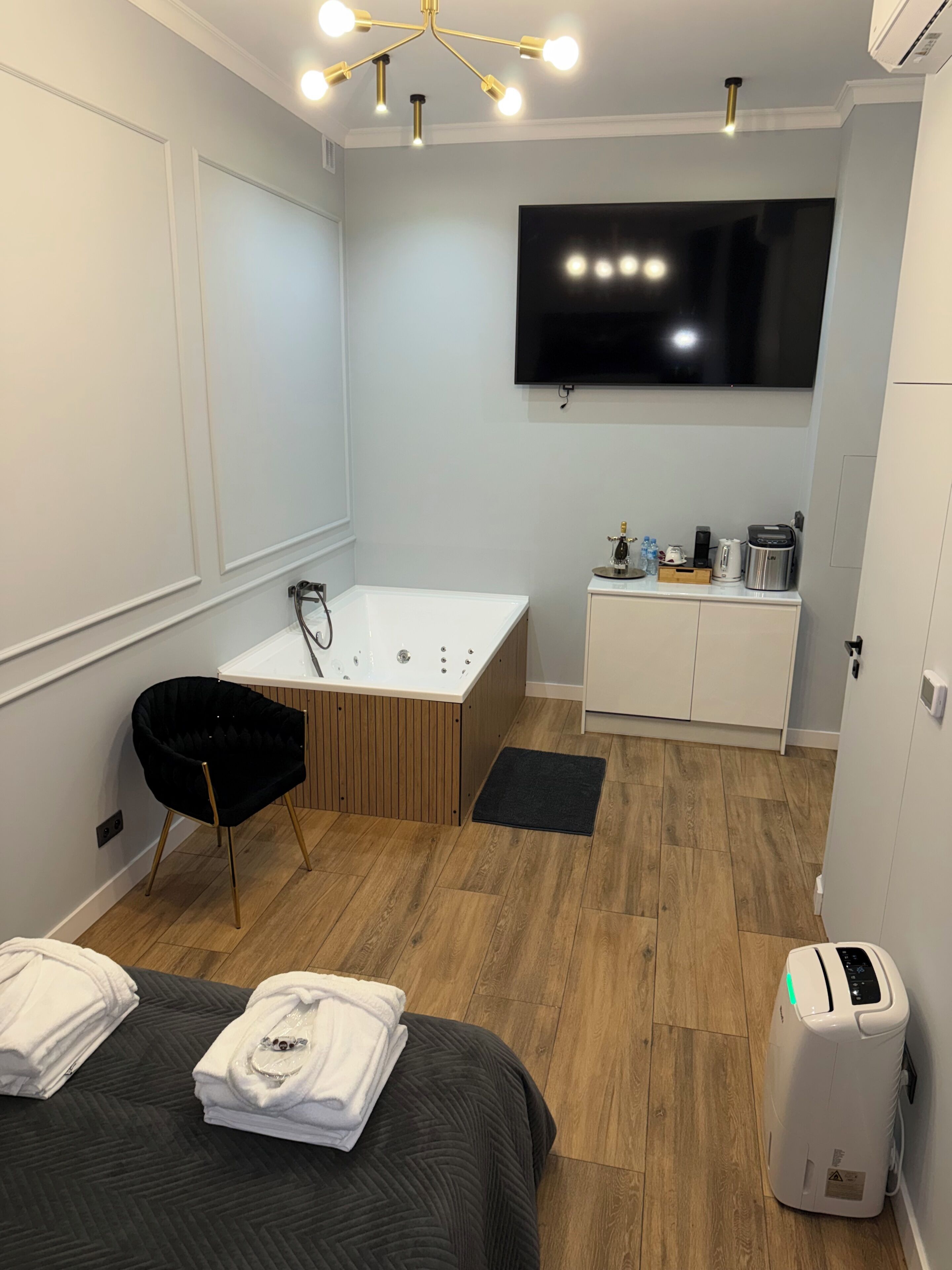 Une salle de bain moderne équipée d’une baignoire, d’un meuble-lavabo, d’un téléviseur à écran plat et d’une chaise noire.