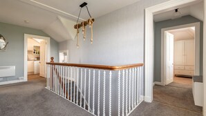 Eine Treppe mit hölzernem Geländer und weißen Spindeln, die zu einem Zwischenpodest mit einer hängenden Leuchte führt.