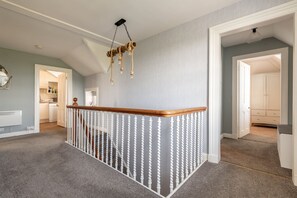 Eine Treppe mit hölzernem Geländer und weißen Spindeln, die zu einem Zwischenpodest mit einer hängenden Leuchte führt.