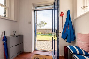 Ein Zimmer mit einer Tür zu einem Außenbereich, einem Bett mit einem gestreiften Kissen, einer blauen Jacke an der Wand und einem kleinen Schreibtisch mit einer Lampe.