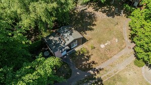 Eine Vogelperspektive zeigt ein Haus, umgeben von dichtem Grün, mit einer auffälligen Auffahrt und einem kleinen Garten.