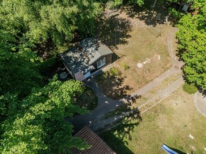 Eine Vogelperspektive zeigt ein Haus, umgeben von dichtem Grün, mit einer auffälligen Auffahrt und einem kleinen Garten.