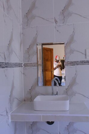 A bathroom with a white sink, a mirror, and a marble wall. - Paradise Reho Guesthouse (Nata)