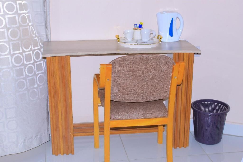 A small wooden desk with a chair, a white kettle, two cups, and a basket.