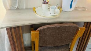 Une chaise en bois avec un siège en osier, une tasse blanche, une soucoupe blanche et une bouilloire blanche posées sur une table en bois.