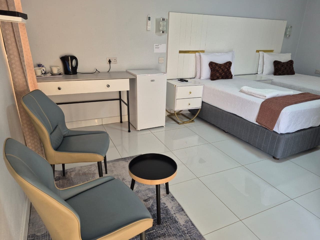 A hotel room with a bed, two chairs, a desk, a small table, and a coffee maker.