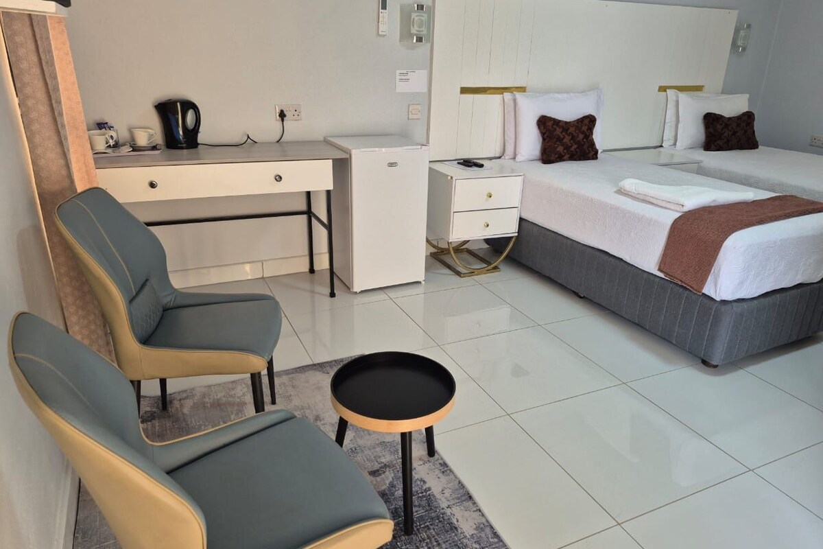 A hotel room with a bed, two chairs, a desk, a small table, and a coffee maker.