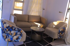 A living room with a sofa, two armchairs, a small round table, and a window with curtains.