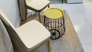 Une petite pièce moderne, avec un réfrigérateur blanc, une petite table sur laquelle se trouve un plateau avec divers objets, une chaise et un tabouret jaune.