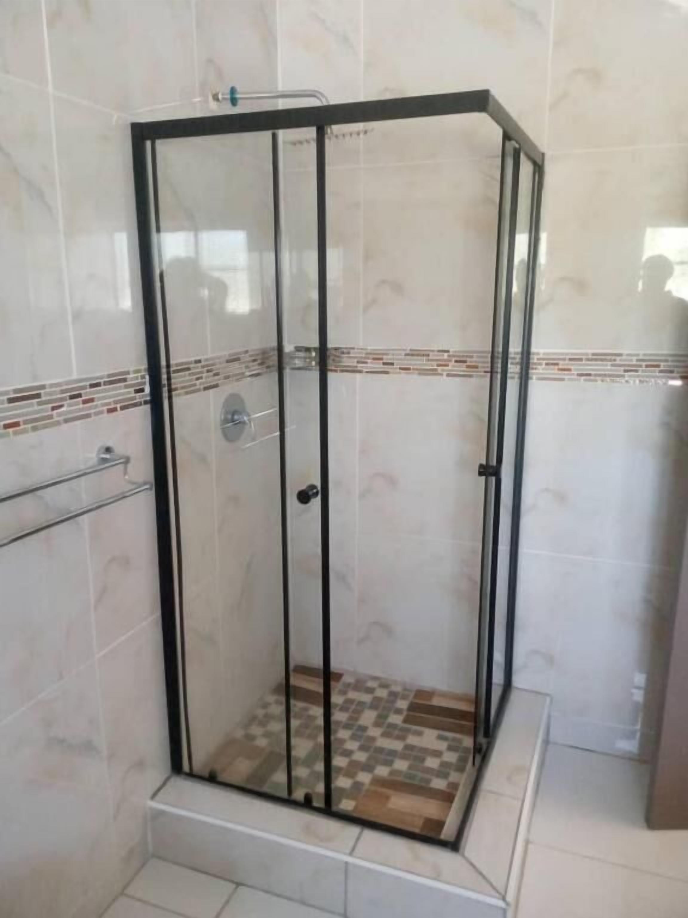 Una ducha con paredes de vidrio, suelo de baldosas y estructura metálica.