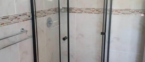 Una ducha con paredes de vidrio, suelo de baldosas y estructura metálica.