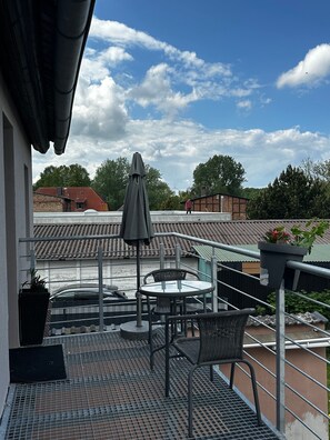 Eine Dachterrasse mit Tisch und Stühlen, einem beschatteten Sonnenschirm und einem Blumentopf.