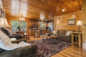 A cozy cabin interior with a wooden ceiling, a dining area, a kitchen, and a living room furnished with a sofa, chairs, and a coffee table. - New Listing | 5BR Gatlinburg Cabin w/ Hot Tub + Game Room + Free Tickets (Gatlinburg)