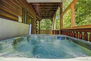 A hot tub in a wooden cabin with a covered deck and a view of trees. - New Listing | 5BR Gatlinburg Cabin w/ Hot Tub + Game Room + Free Tickets (Gatlinburg)