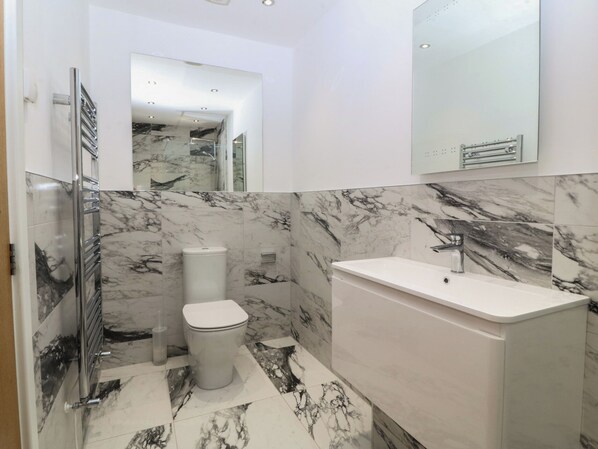 A bathroom with a white toilet, a white sink, and a mirror above the sink. - Hillside (Tyn-y-Gongl)