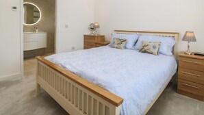 A bedroom with a bed, bedside tables, a nightstand, a mirror, and a bathroom with a sink and toilet. - Hillside (Tyn-y-Gongl)