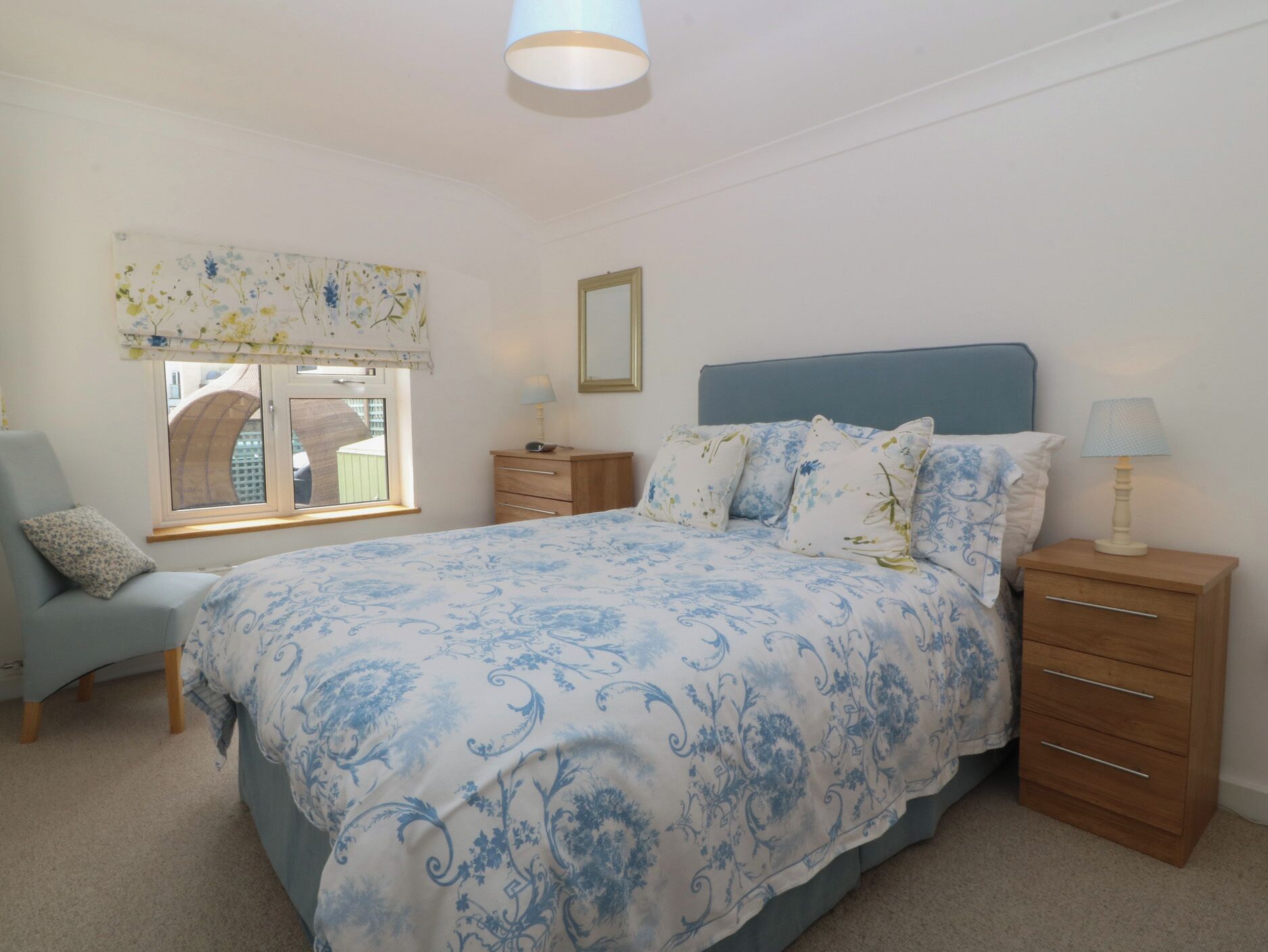A bedroom with a bed, a chair, a nightstand, a lamp, a window, and a wall decoration.