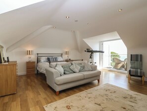A spacious loft bedroom with a large bed, a telescope, and a balcony with wicker furniture. - Hillside (Tyn-y-Gongl)