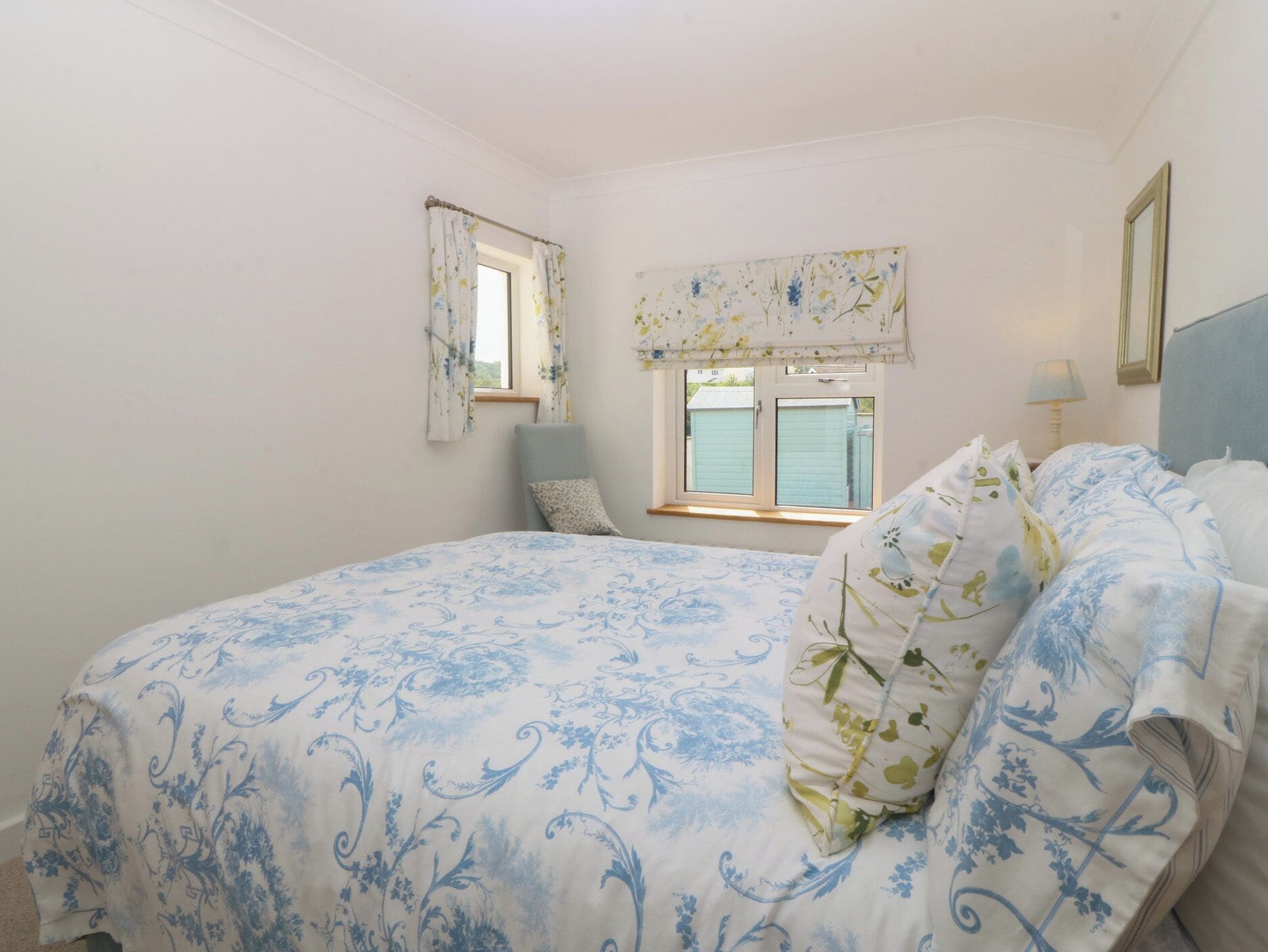 Une chambre avec un grand lit, une fenêtre avec des rideaux, une chaise et une table de chevet.