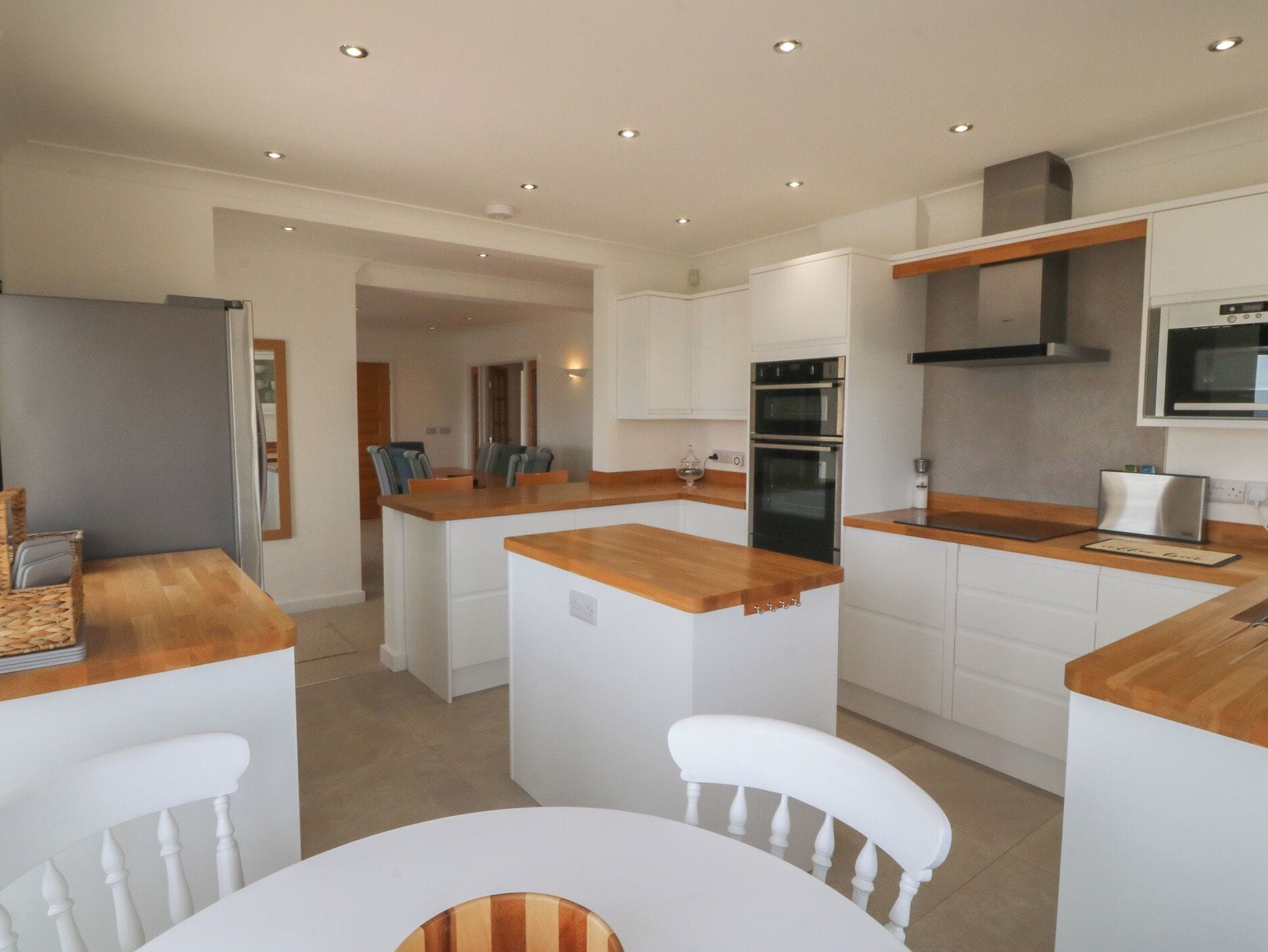 A modern kitchen with white cabinetry, wooden countertops, and a central island with seating.