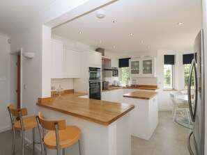 Una cocina moderna con armarios blancos, una isla de madera y un comedor con sillas.
