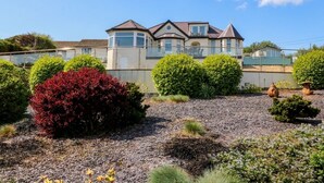 A large house with a balcony, surrounded by well-maintained gardens and a gravel driveway. - Hillside (Tyn-y-Gongl)