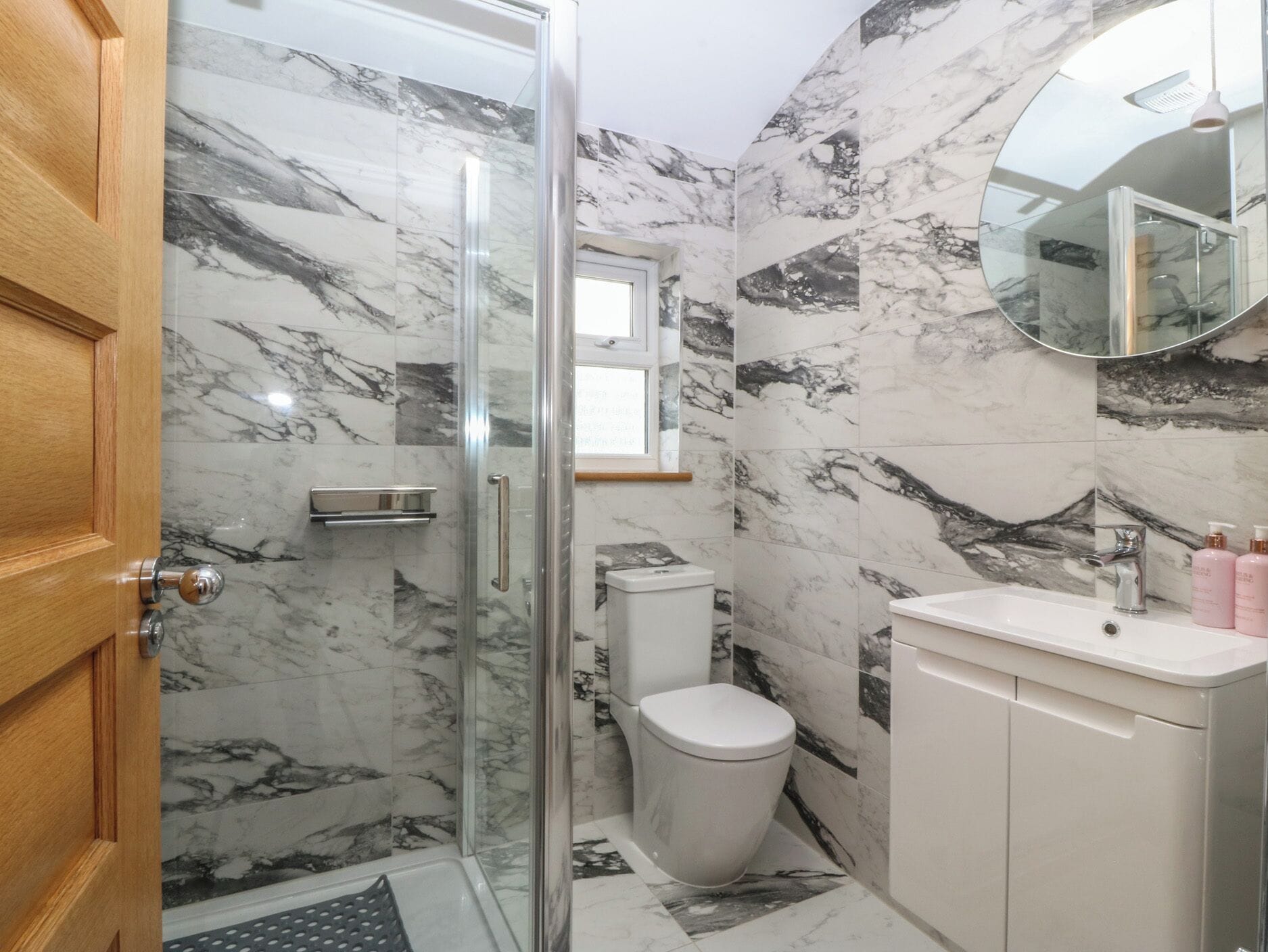A bathroom with a glass shower enclosure, a toilet, a sink with a mirror, and marble-patterned walls.