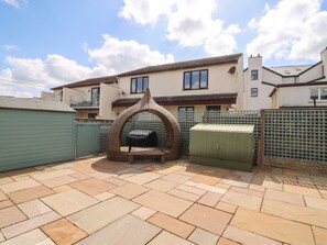 A patio with a barbecue grill, a green storage unit, and a fence. - Hillside (Tyn-y-Gongl)