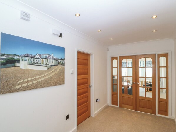A hallway with a wooden door, a glass door with a view, and a painting on the wall. - Hillside (Tyn-y-Gongl)