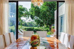 Ein Essbereich mit einem Glastisch, Stühlen und Blick auf einen Garten und Pool.