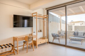 Ein modernes Zimmer mit Schreibtisch aus Holz, Stuhl und Fernseher. Es gibt einen Balkon mit Sitzgelegenheit im Freien.