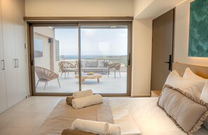 Ein Schlafzimmer mit einem großen Bett und einer Glastür, die auf einen Balkon mit Sitzmöbeln führt.