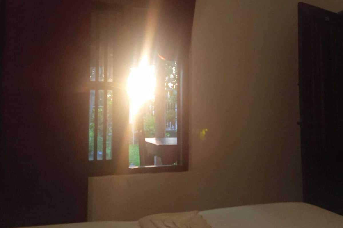 Una habitación tenuemente iluminada con una cama, una ventana con cortinas y una puerta.