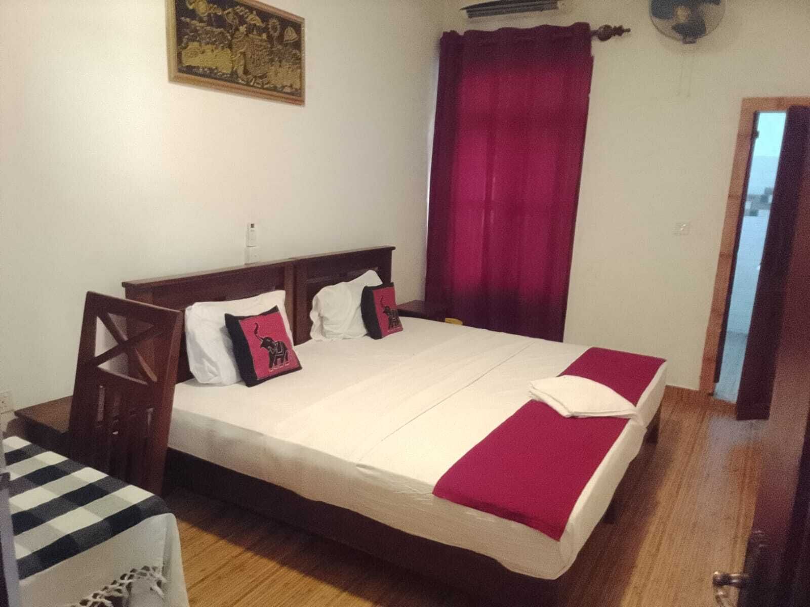 Una habitación de hotel estándar con cama, mesita de noche, silla y ventana con cortinas.