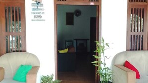 A room with a wooden floor, two armchairs with cushions, a potted plant, and a doorway leading to another room. - Rio Lake Hotel Sigiriya (Sigiriya)