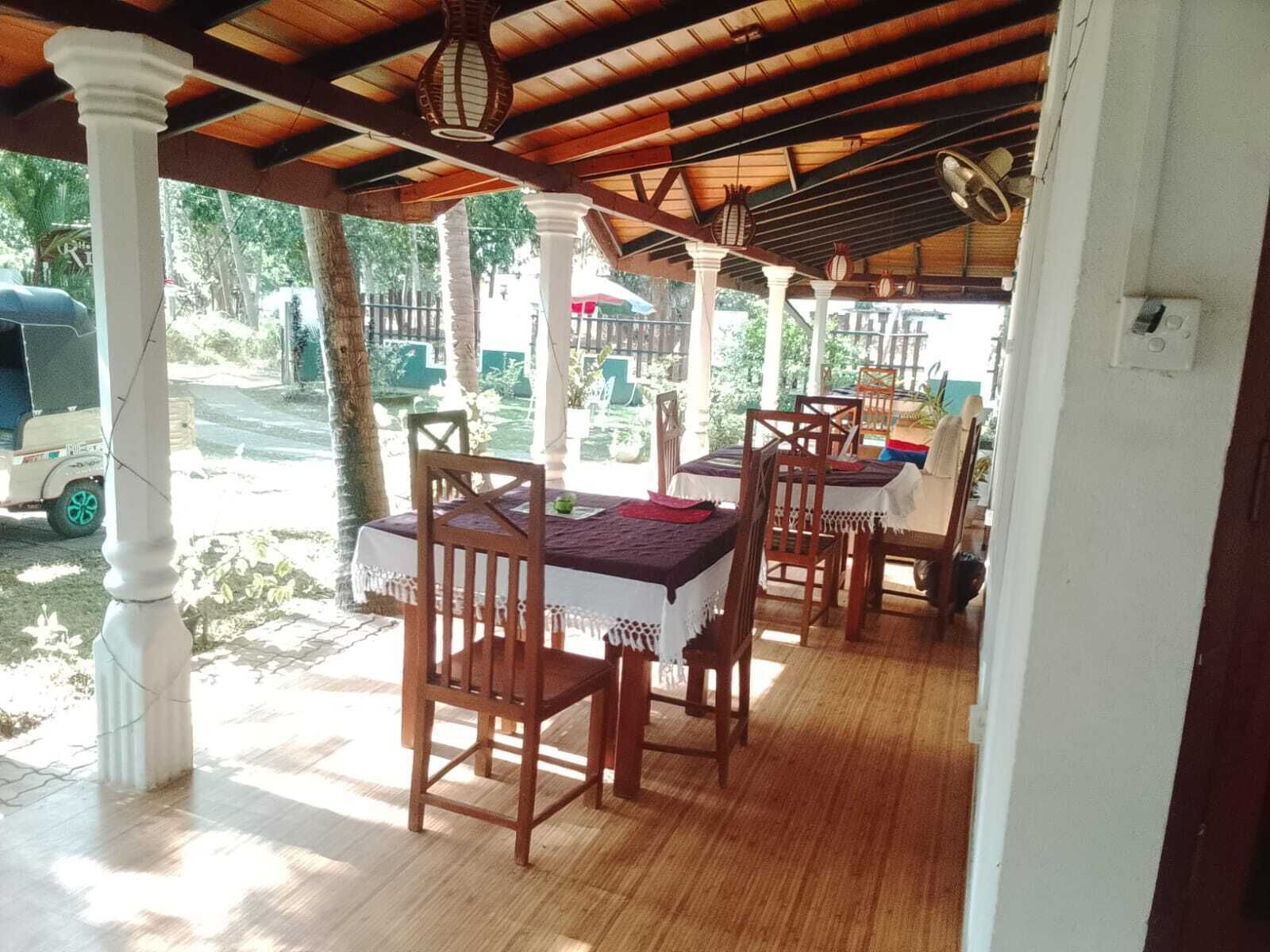 Un espace de restauration extérieur abrité, avec des tables et des chaises en bois, une balustrade blanche et une vue sur les environs.