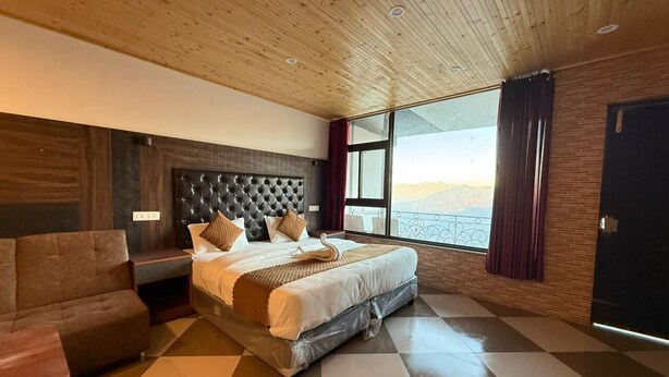 Une chambre d’hôtel moderne avec un grand lit, un canapé, un plafond en bois et une vue sur l’extérieur.