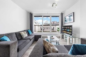 A modern living room with a grey sofa set, a glass coffee table, and a flat-screen TV. - Zone 2 Serviced apartment by the River Thames (London)