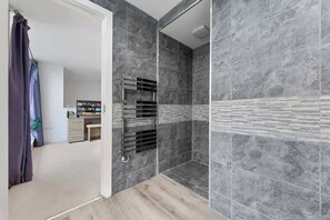 A modern bathroom with grey tiles, a shower area, and a visible bathroom counter with a towel rack. - Zone 2 Serviced apartment by the River Thames (London)