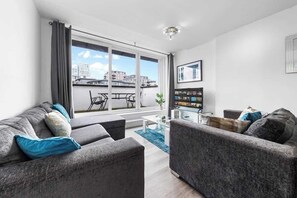 Een moderne woonkamer met een groot raam, grijze banken, een salontafel en een bijzettafeltje.