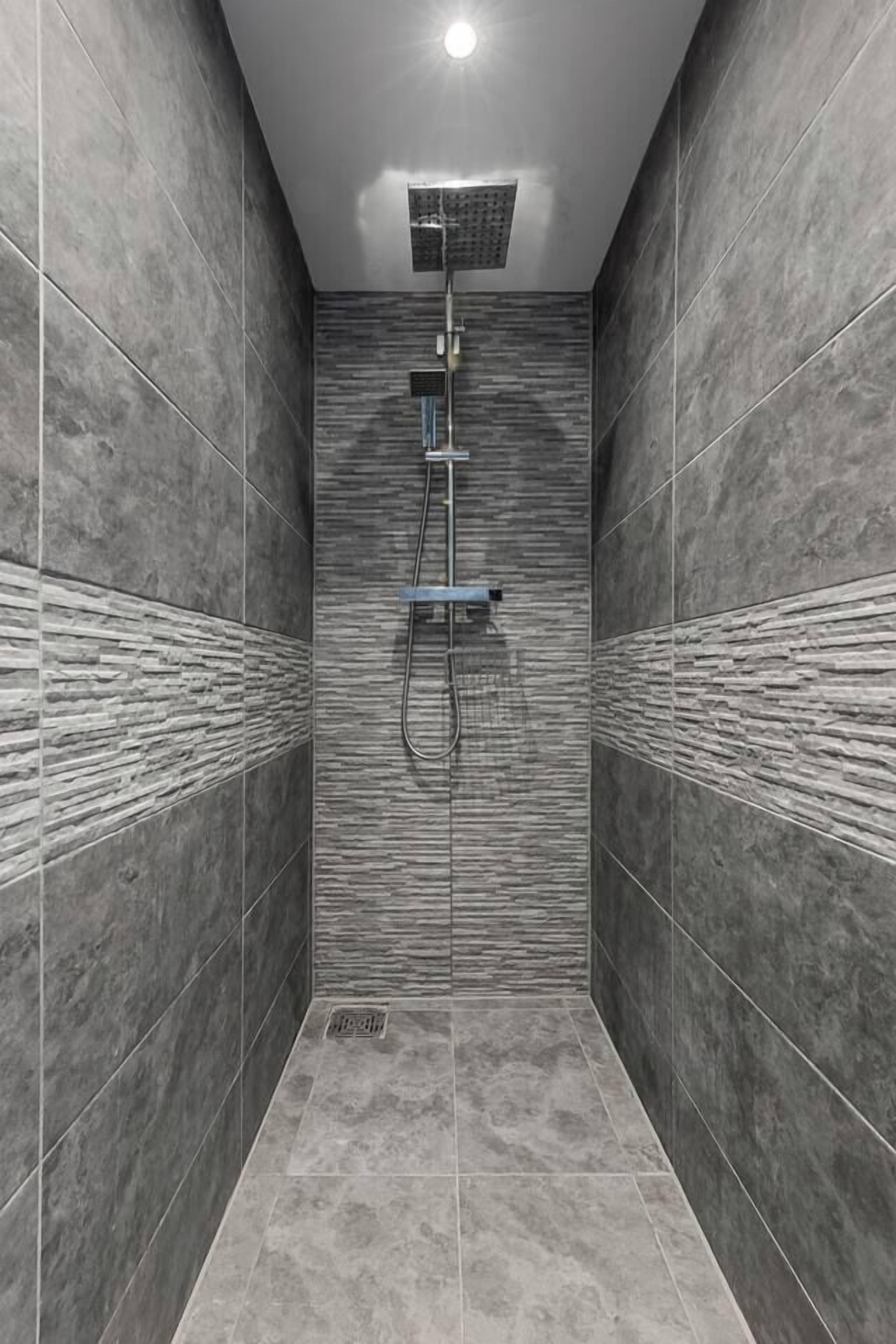 A narrow shower stall with a modern showerhead and a rectangular mirror.