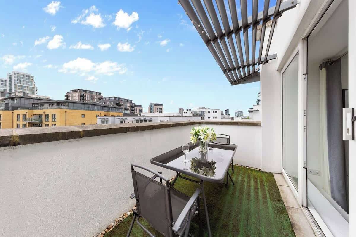 A rooftop terrace with a table and chairs, a view of the cityscape, and a pergola structure.